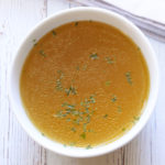 Homemade chicken broth is served in a white bowl.