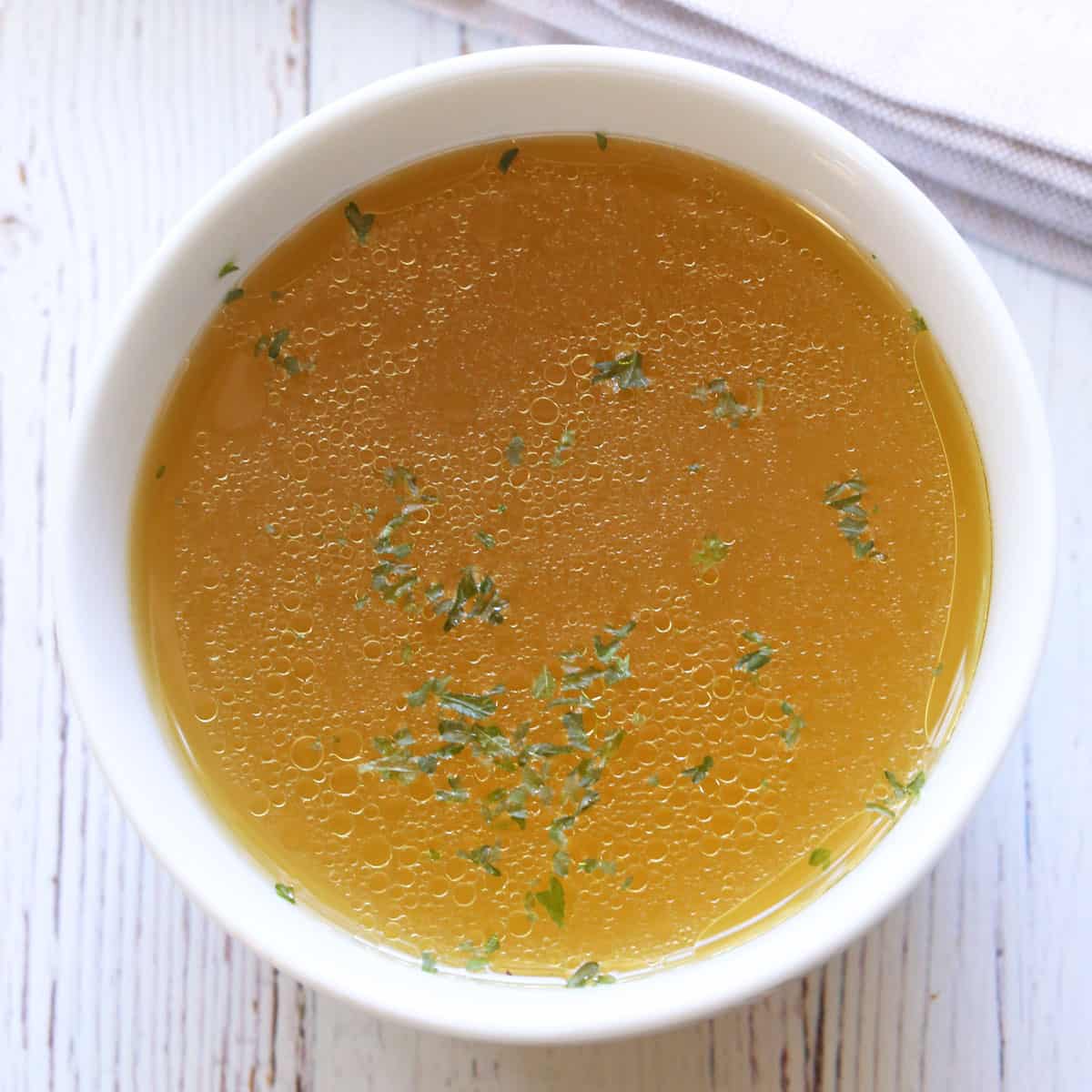 Homemade chicken broth is served in a white bowl.
