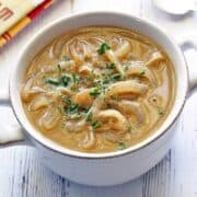 Onion soup is served in a white bowl with a spoon and a napkin.