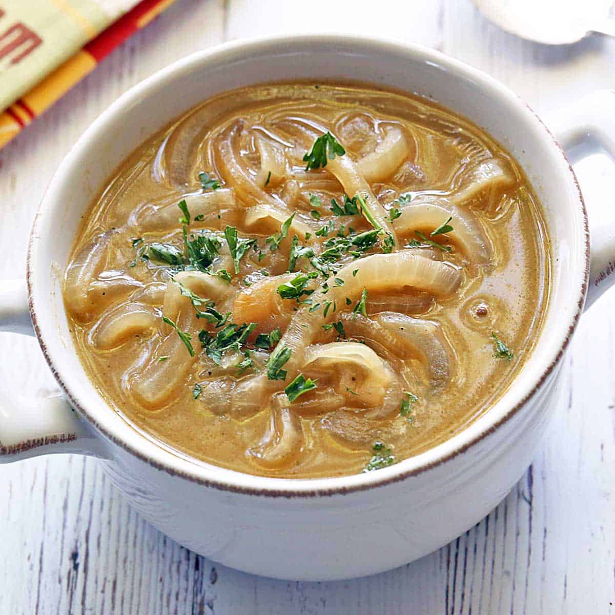 Onion soup is served in a white bowl with a spoon and a napkin.
