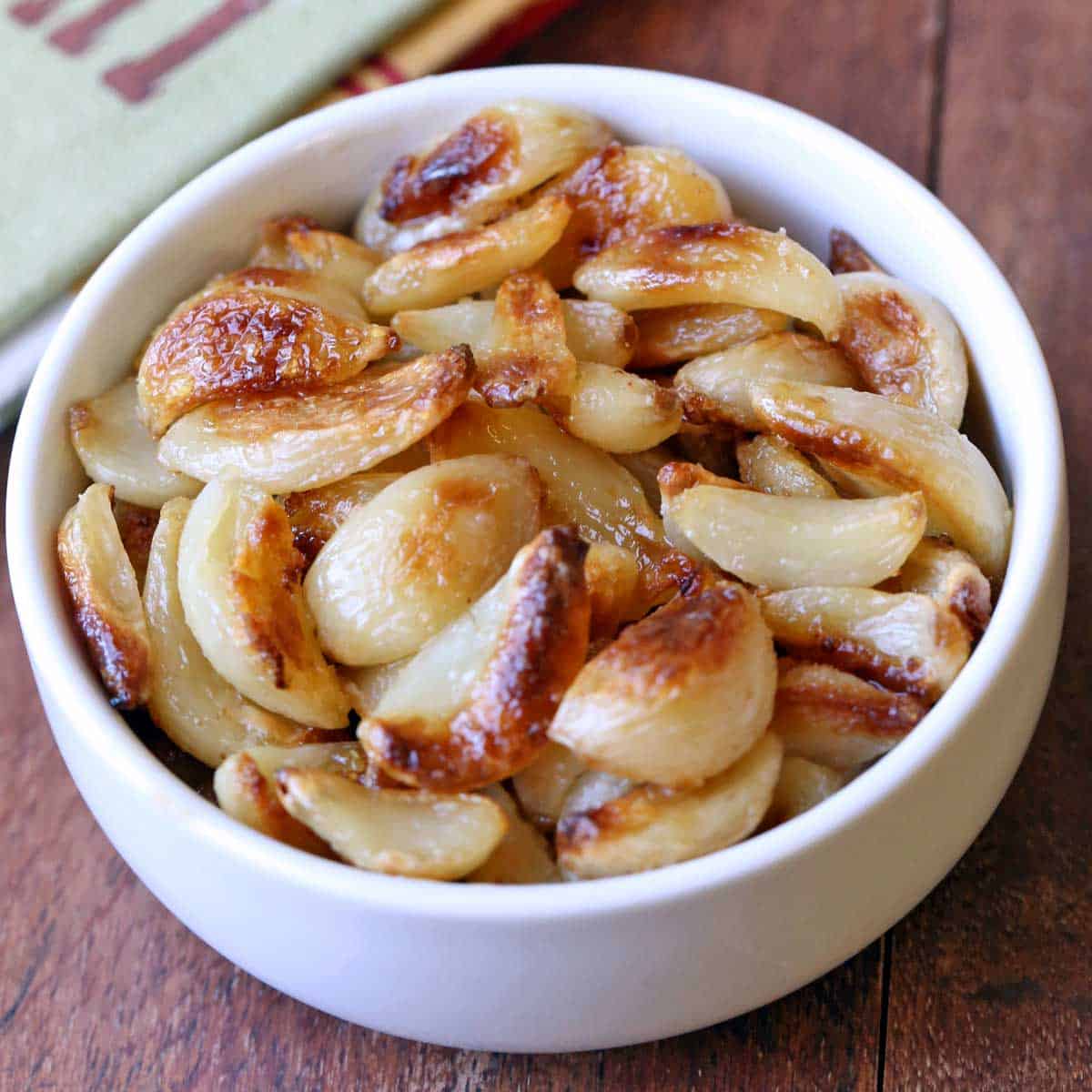 Roasted garlic cloves are served in a white bowl with a napkin.
