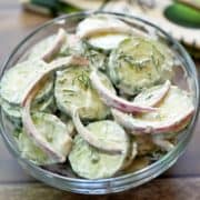 Cucumber salad with sour cream is served in a glass bowl.