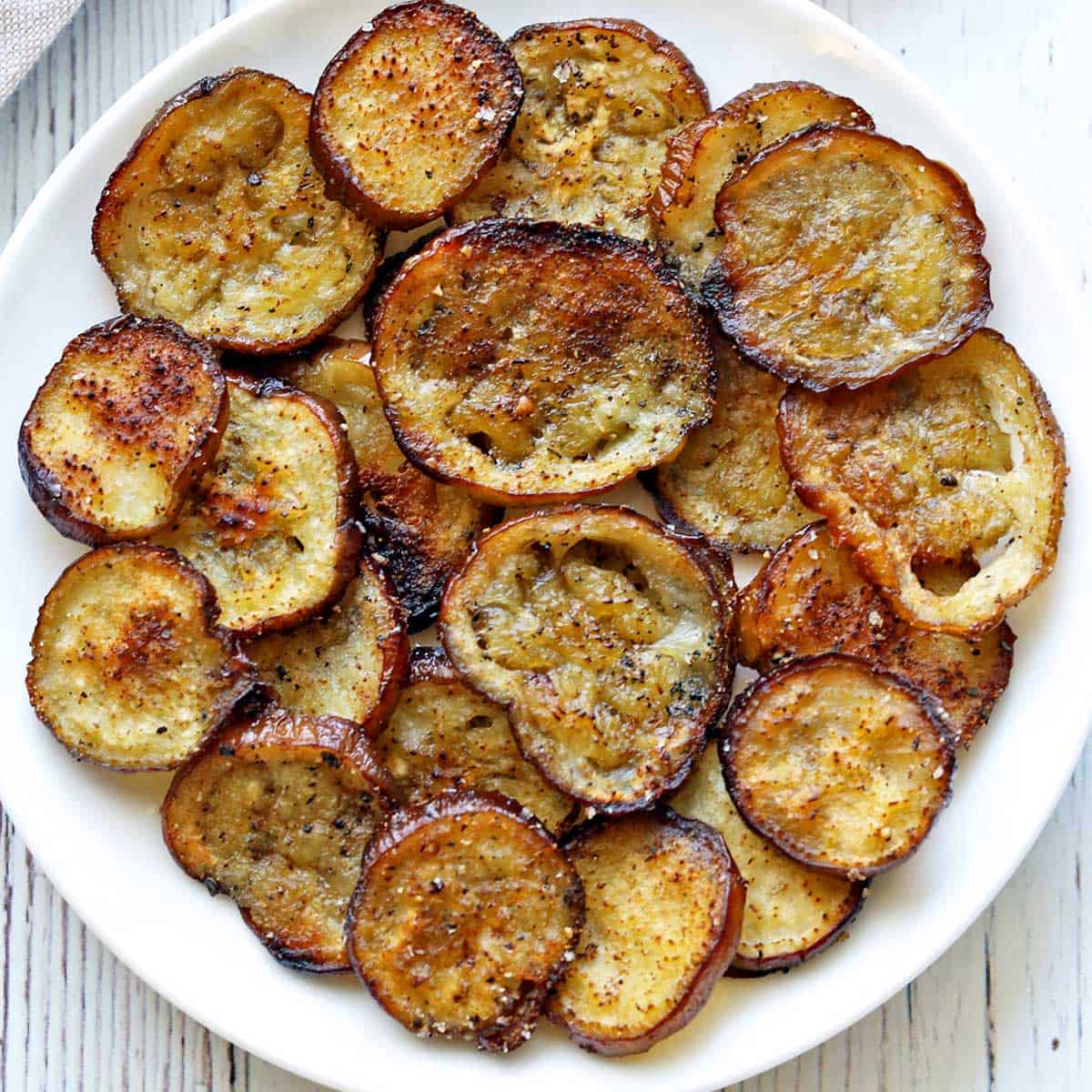 Eggplant chips are piled on a white plate.