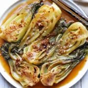 Sauteed bok choy is served on a white plate with chopsticks.