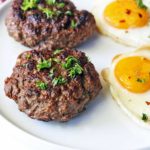 Beef sausage is served on a white plate with fried eggs.