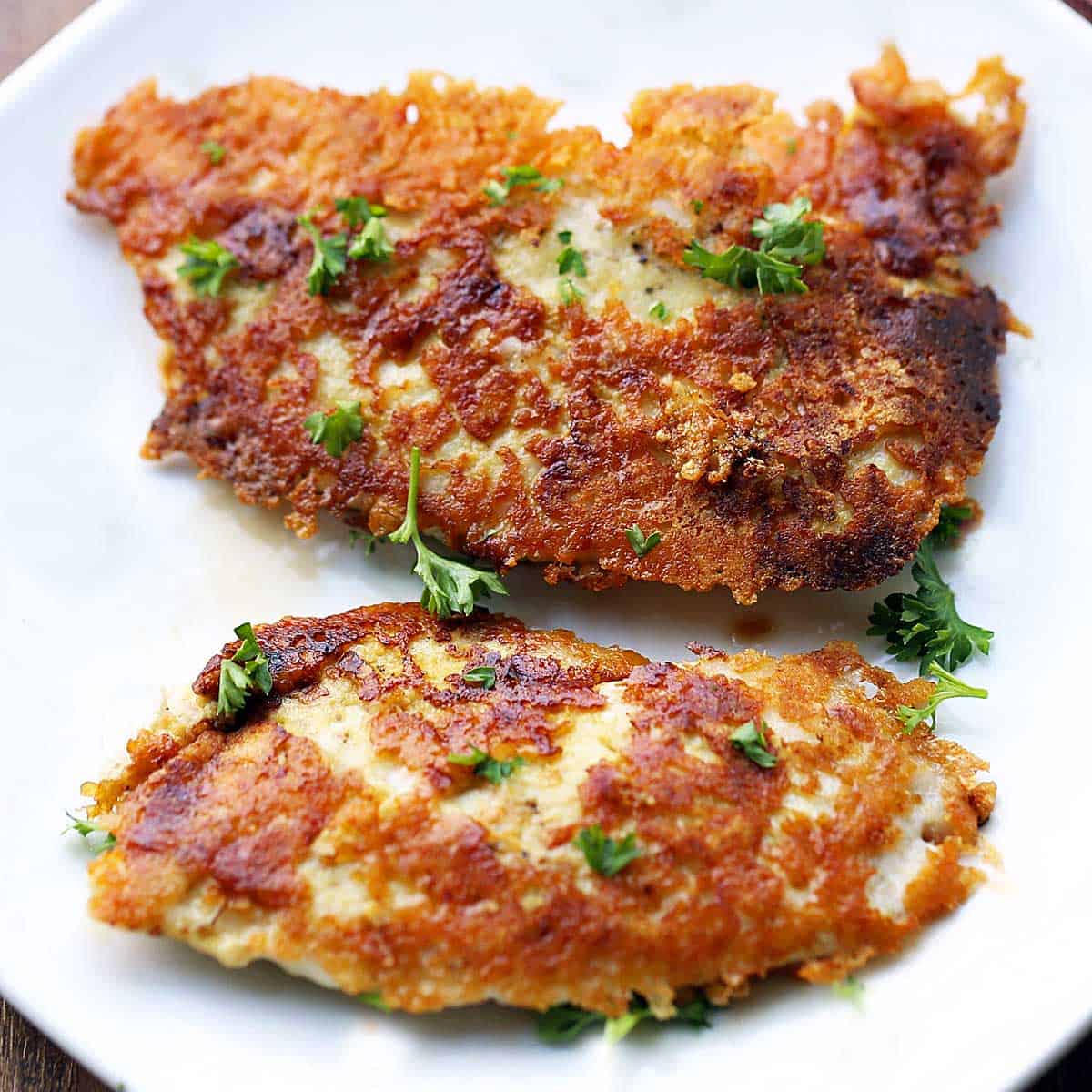 Parmesan chicken tenders are served on a white plate.