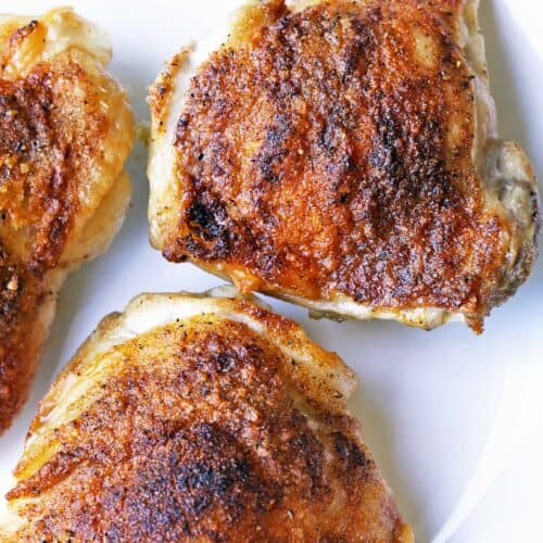 Crispy chicken thighs are served on a white plate.
