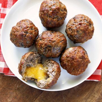 Cheese stuffed meatballs are served on a white plate with a napkin.
