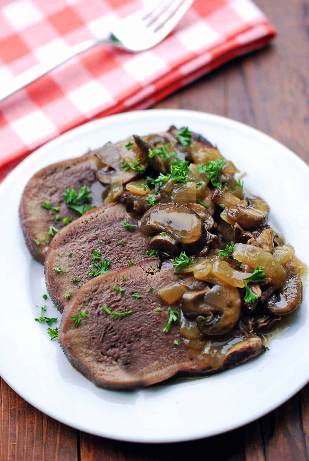 Slices of beef tongue are served on a white plate with a napkin. 