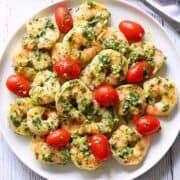 Pesto shrimp is served with tomatoes on a white plate.