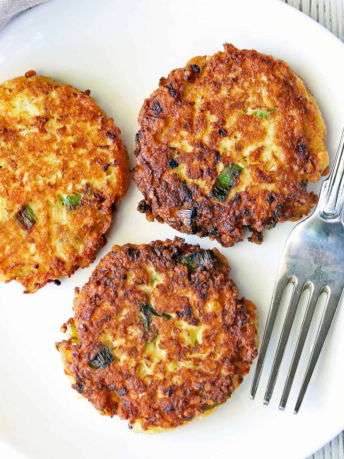 Three cauliflower fritters served on a white plate. 