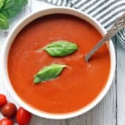 Tomato soup is served in a white bowl with a spoon.