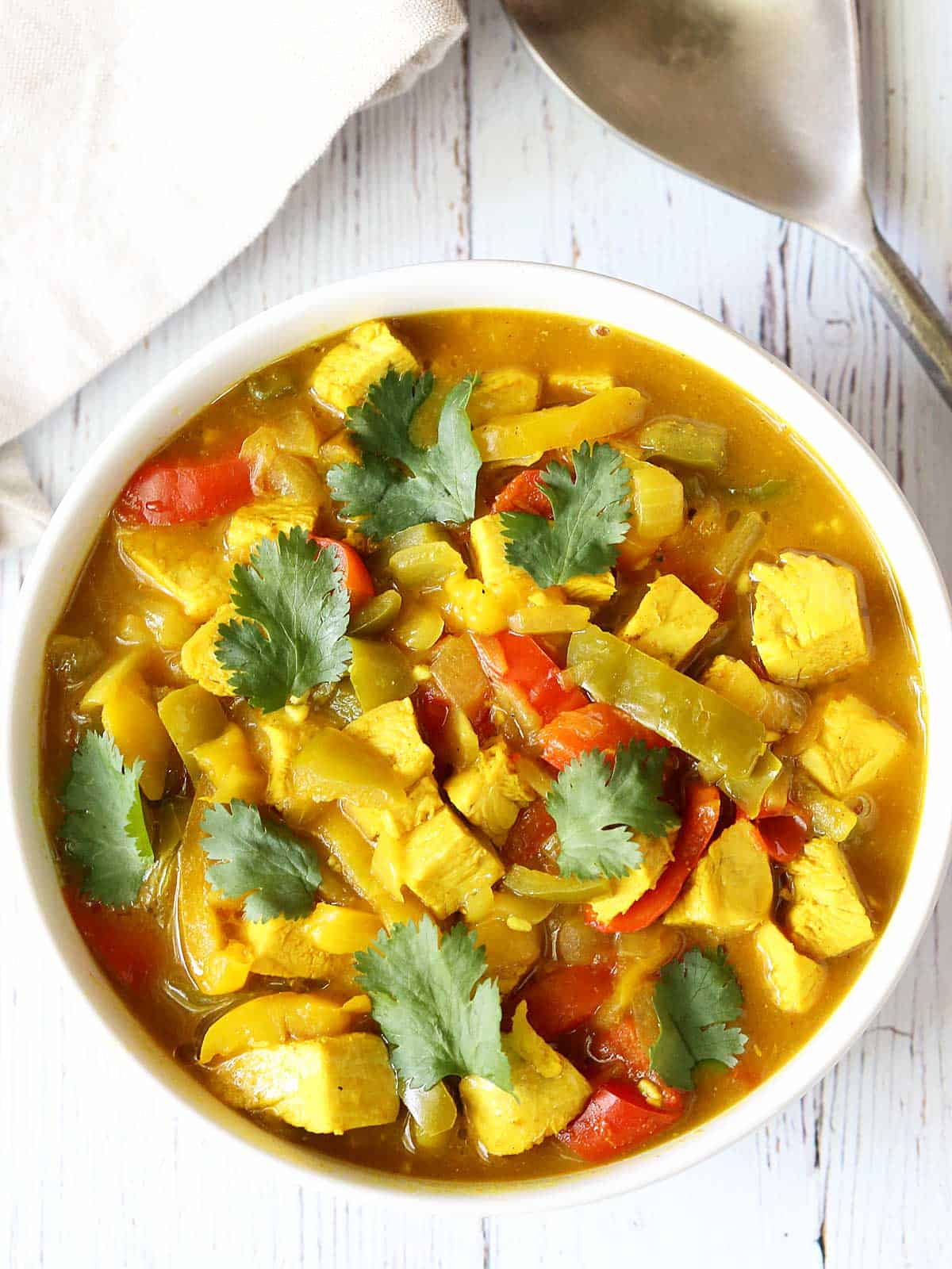 A bowl of turkey curry is served with a spoon and a napkin. 