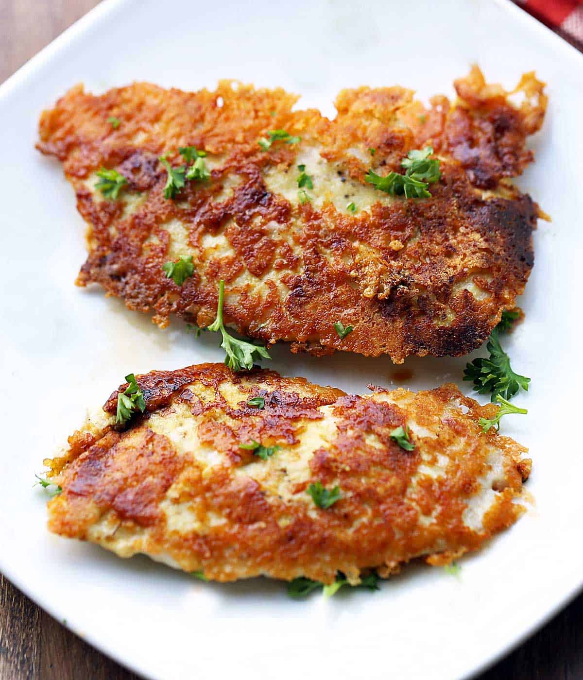 Parmesan chicken tenders are served on a white plate. 