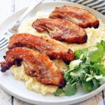 Pork jowls are served on a white plate with a fork.