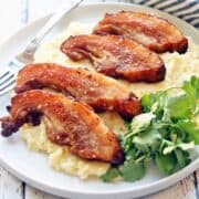 Pork jowls are served on a white plate with a fork.