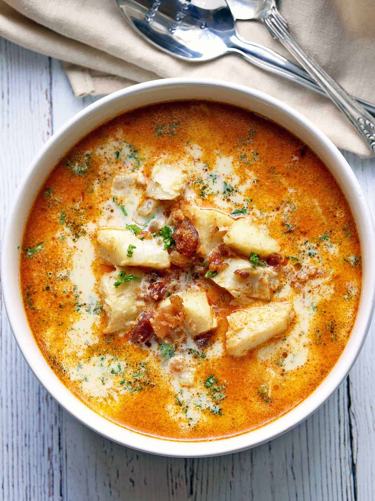 Keto fish chowder is served in a white bowl with spoons. 