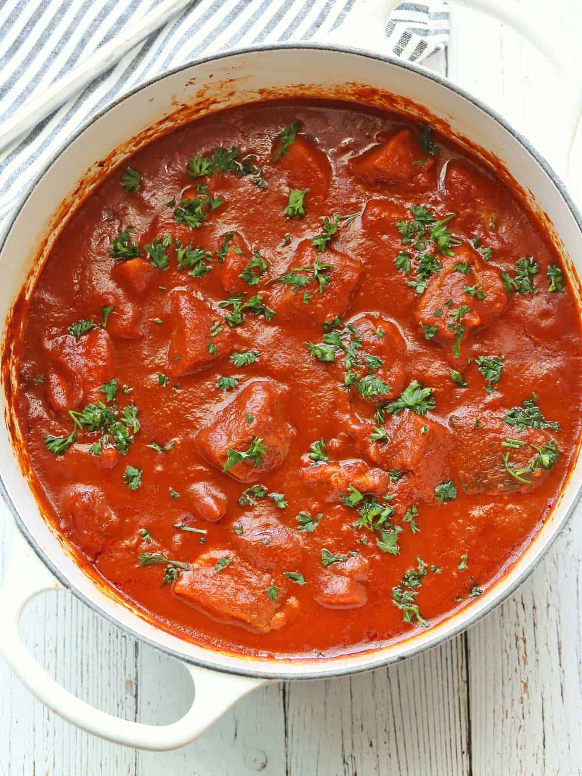 A fish stew served in a white saucepan and topped with chopped parsley. 
