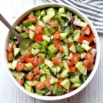 Israeli salad is served in a white bowl with a serving spoon.