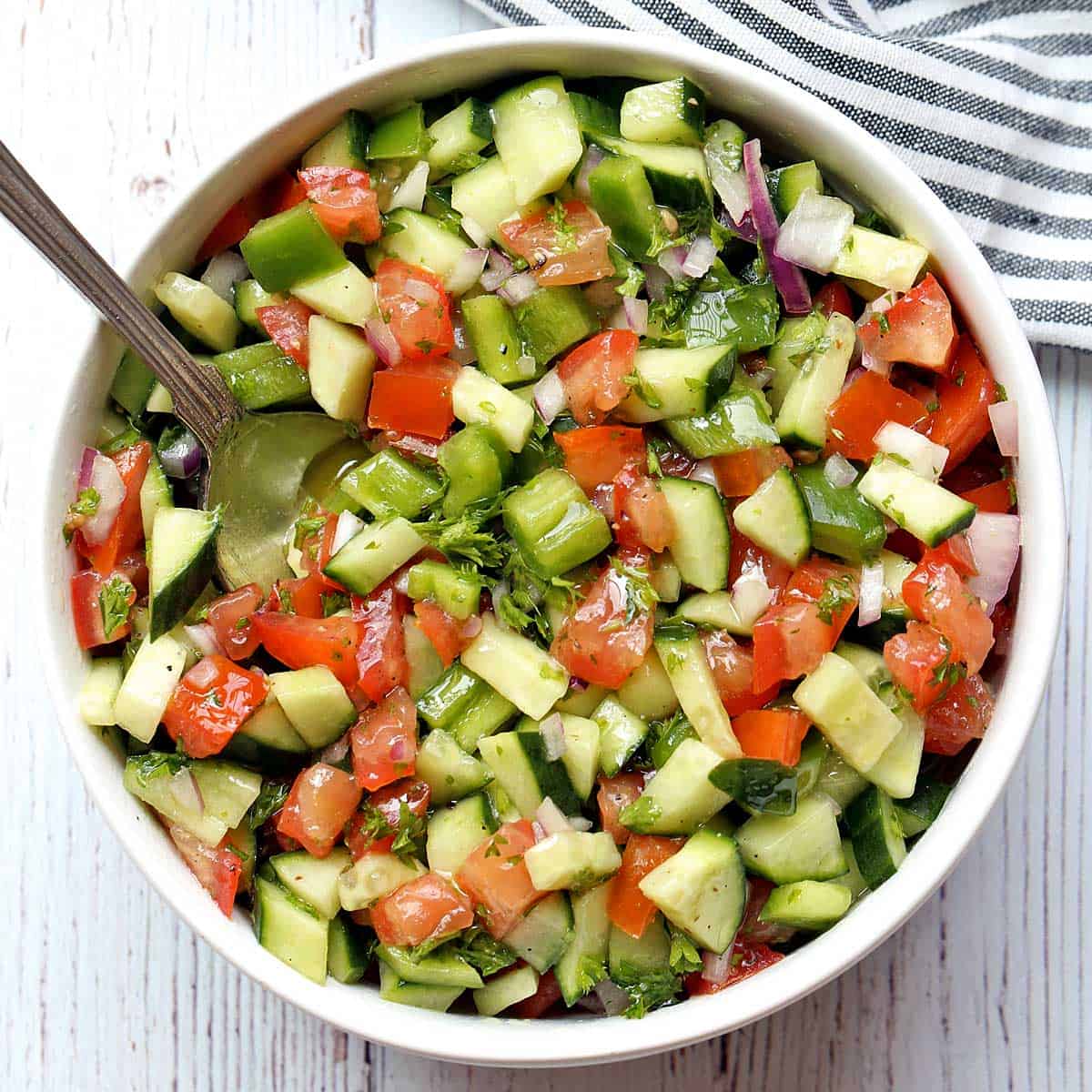Israeli salad is served in a white bowl with a serving spoon.