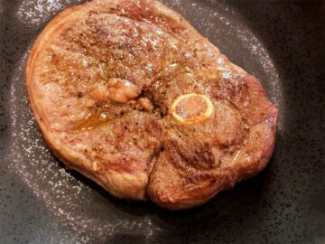 Lamb steak is served on a black dinner plate.