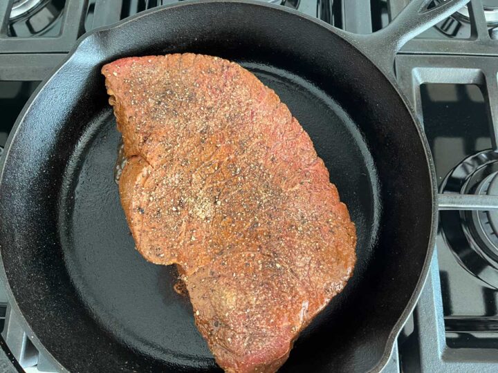 Cooking the London broil on the first side on a cast-iron skillet.