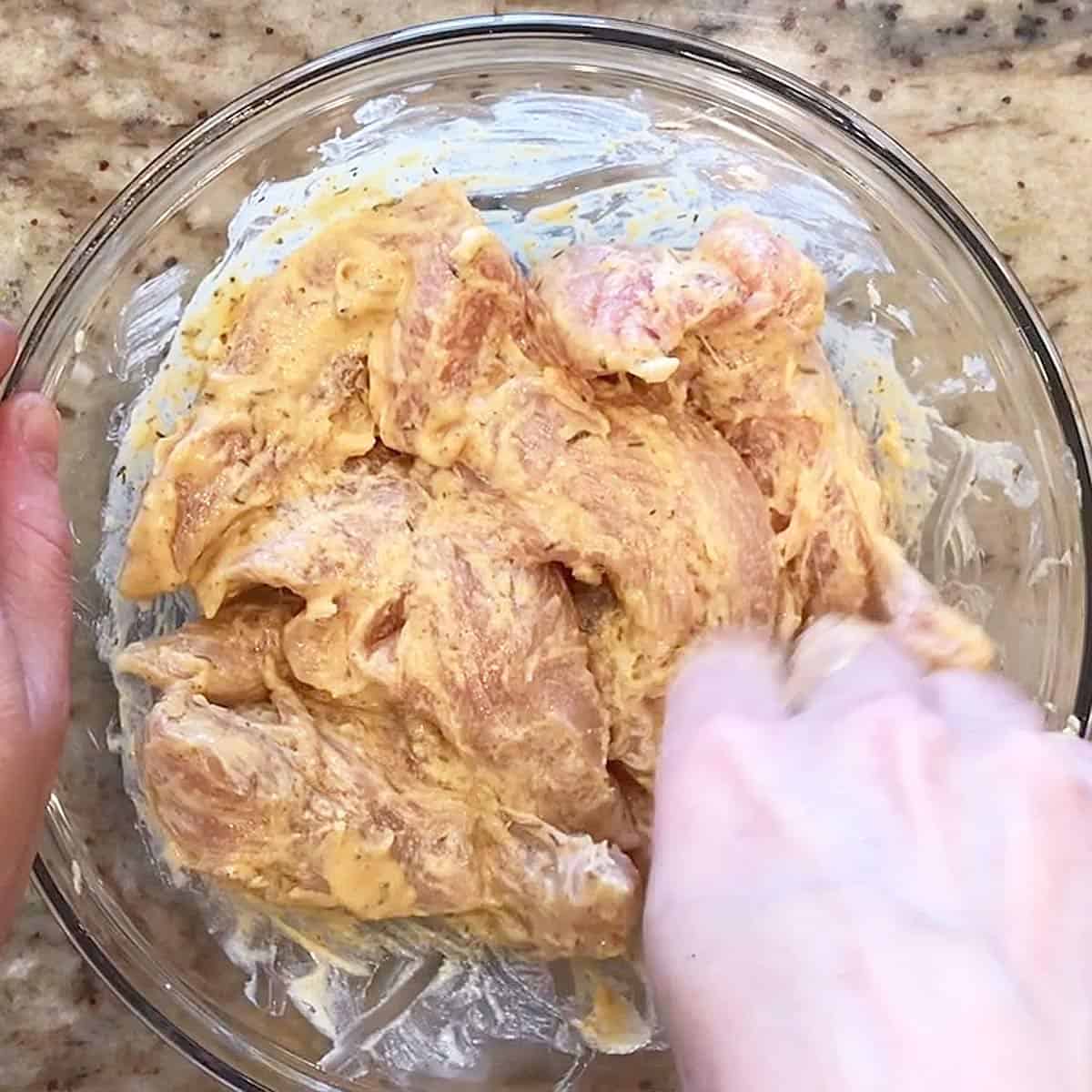 Coating the chicken pieces in the mayo-mustard mixture.