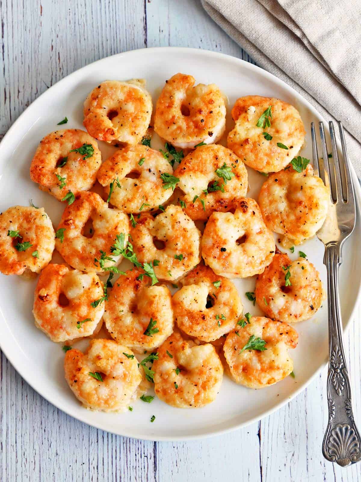 Shrimp parmesan are served on a white plate with a fork. 
