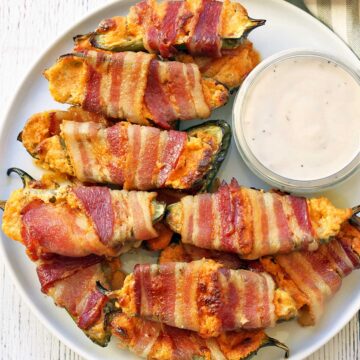 Stuffed jalapenos are served on a plate with a dip.