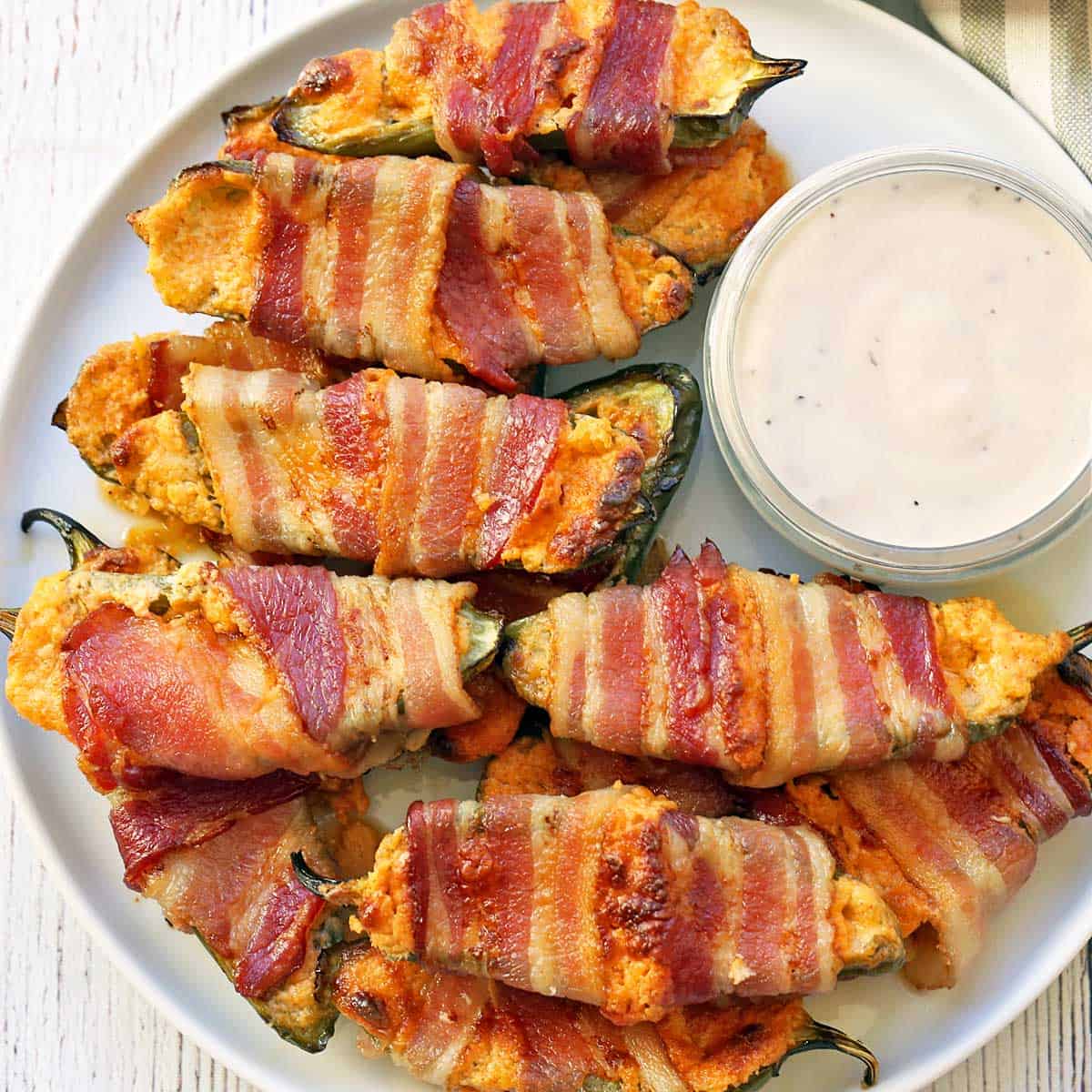 Stuffed jalapenos are served on a plate with a dip.