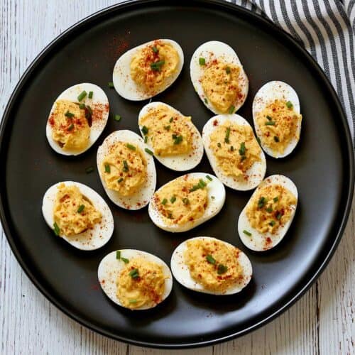Deviled eggs are served on a black plate with a striped napkin.