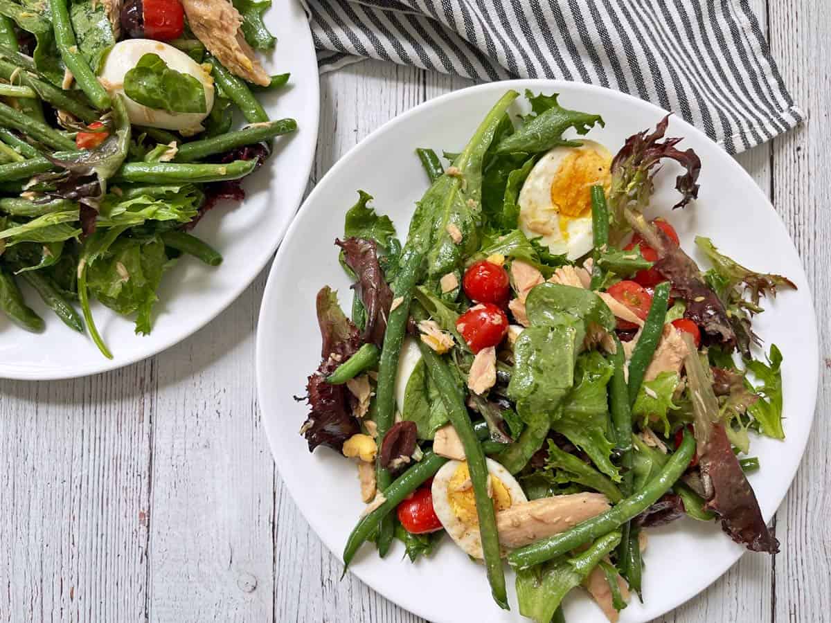 Two dinner plates with nicoise salad.