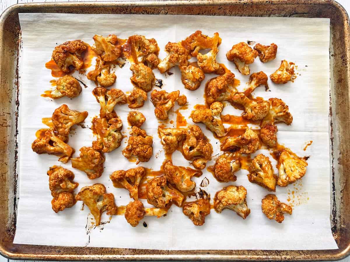 Buffalo cauliflower is ready on a parchment-lined baking sheet.