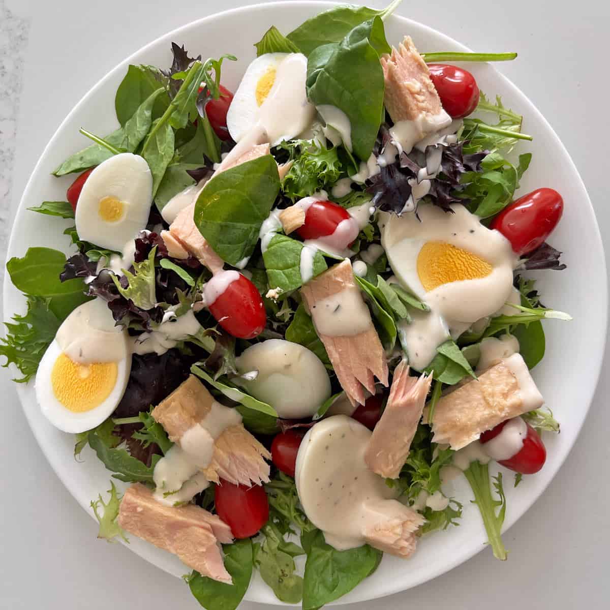 A lazy version of Nicoise salad with lettuce, tomatoes, eggs, tuna, and store-bought dressing.