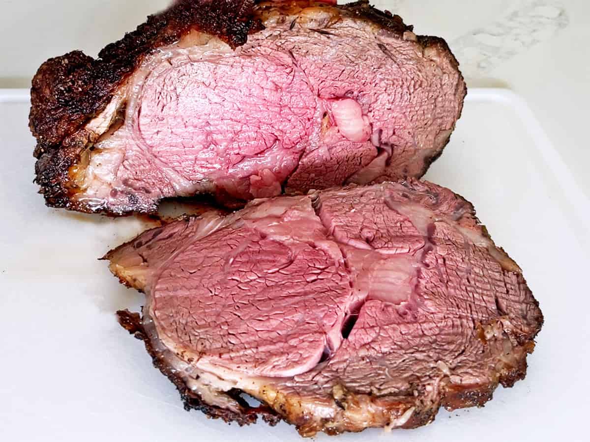 A sliced ribeye roast is served on a white cutting board.