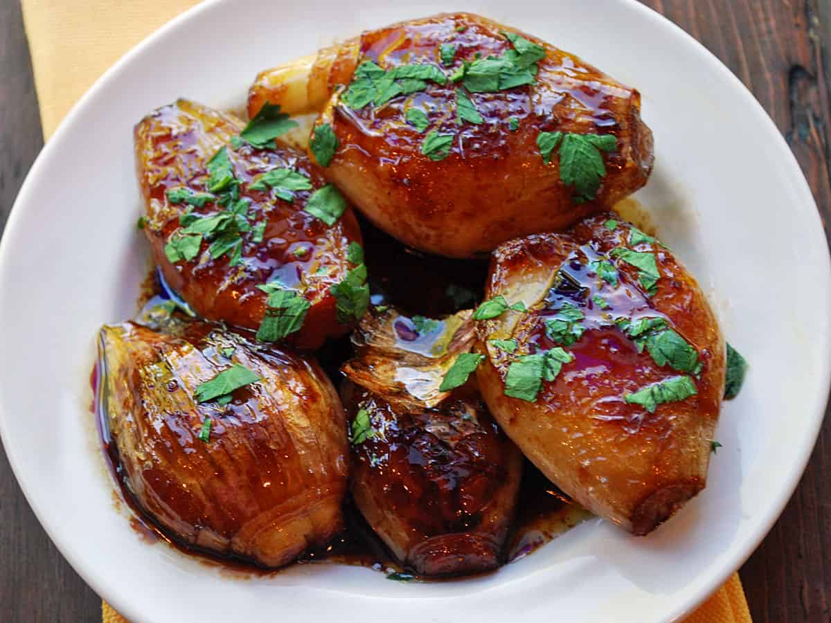 Caramelized shallots are served in a white bowl, topped with chopped parsley.