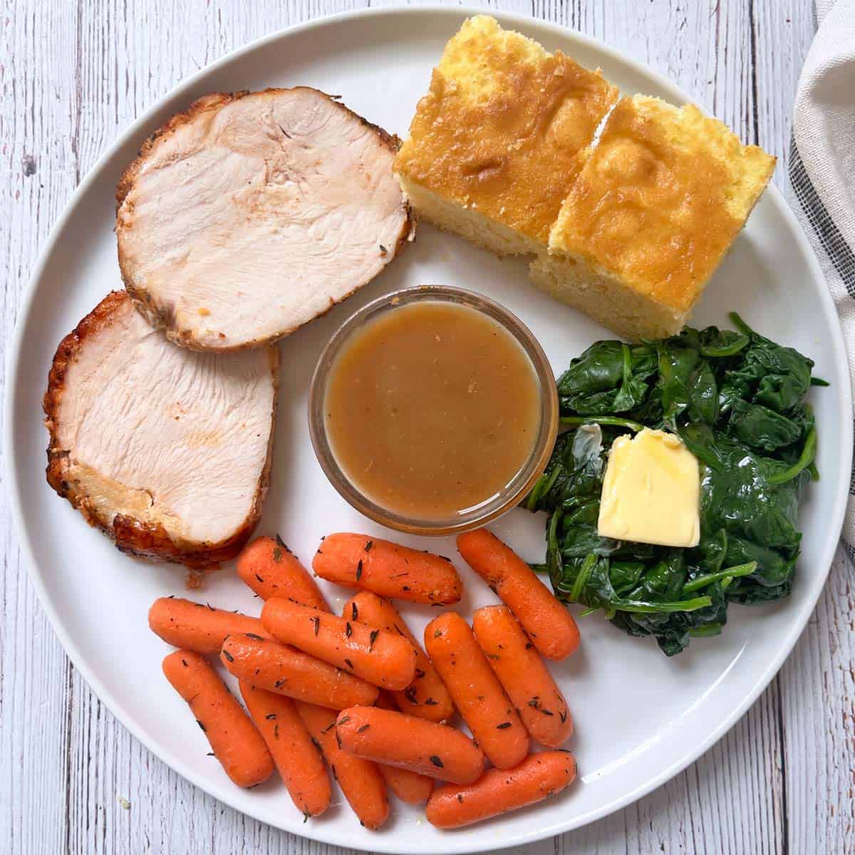 Roasted turkey breast is served with gravy, carrots, spinach, and cornbread.