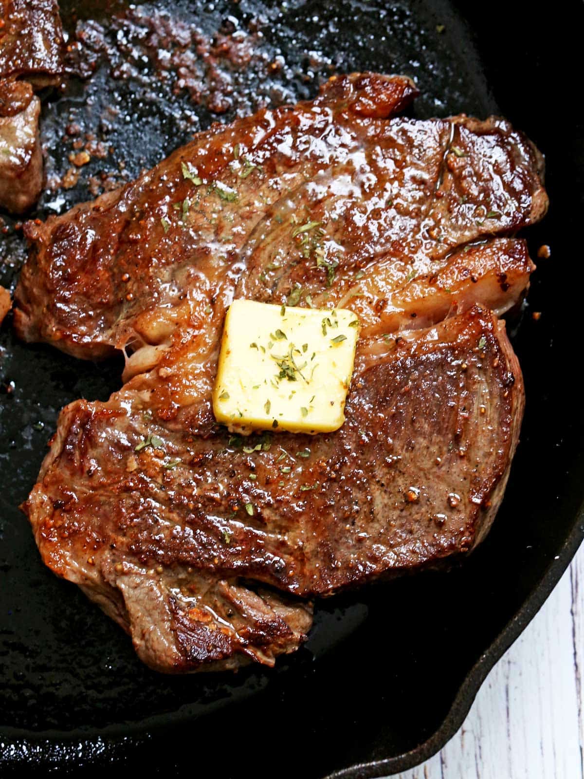 A chuck eye steak in a cast-iron skillet is topped with butter.