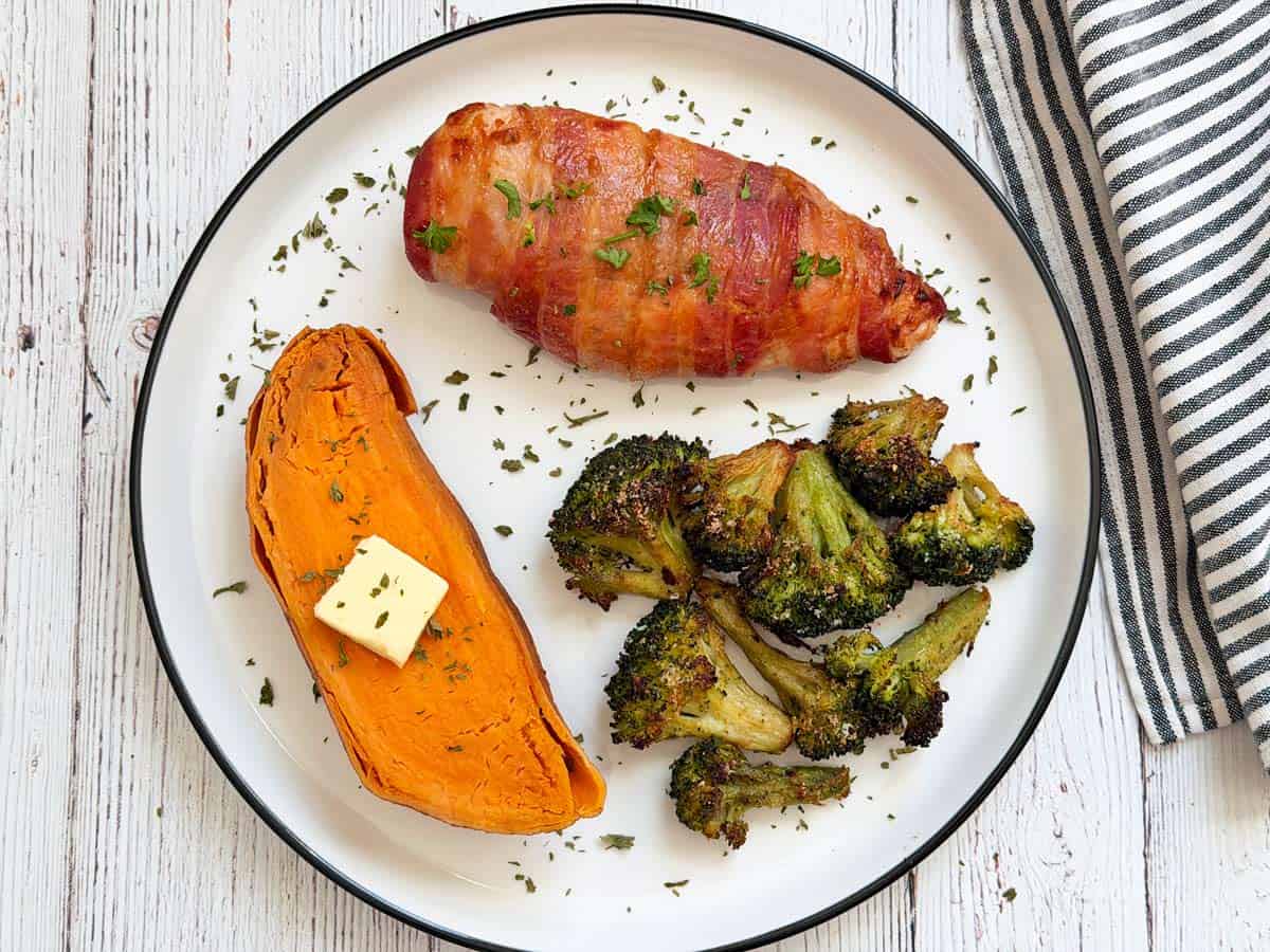 A microwave sweet potato is served with bacon wrapped chicken and roasted broccoli.