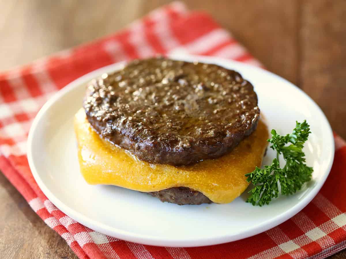 A bunless cheeseburger is served on a white plate with a red napkin.