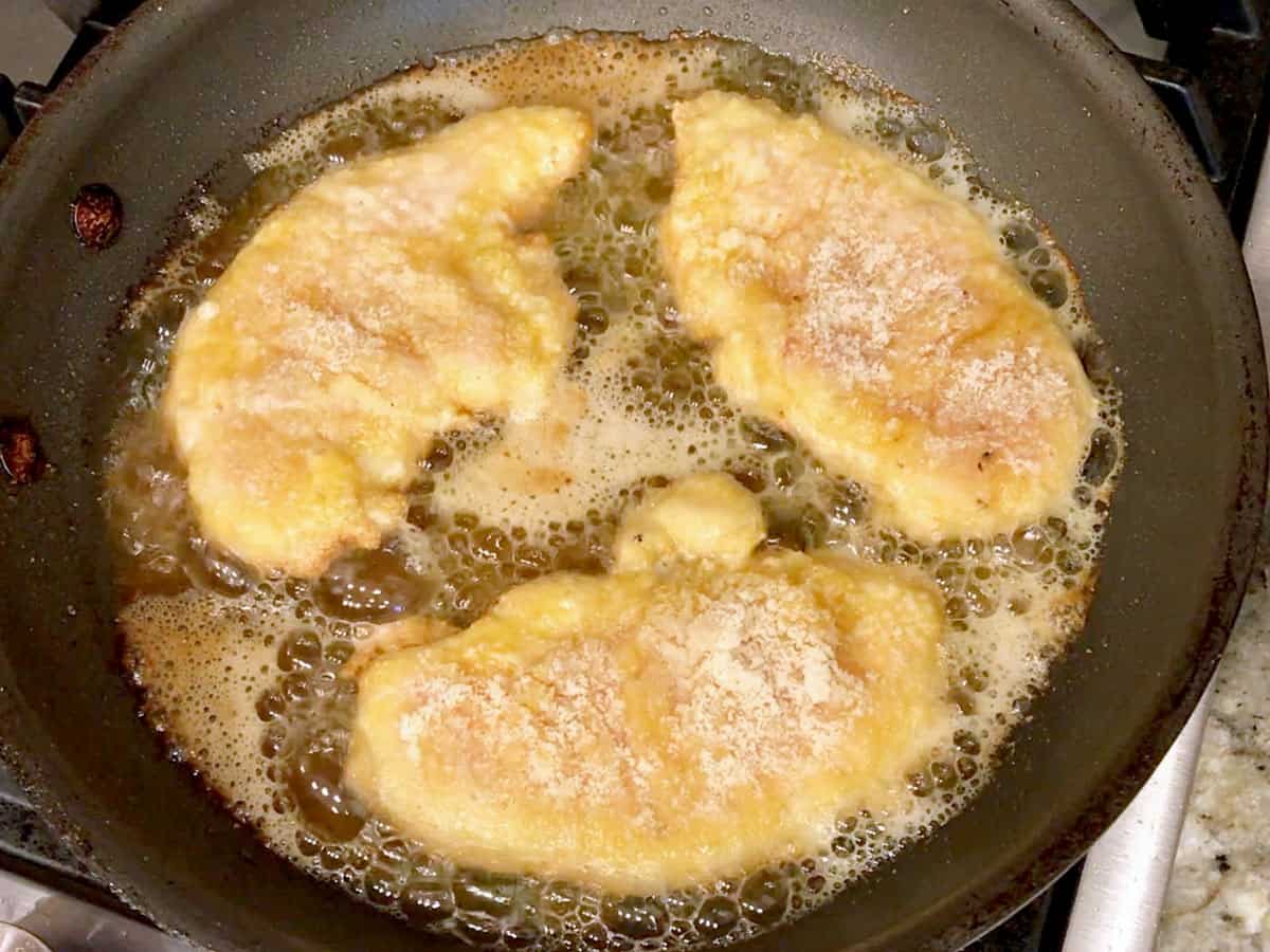 Three almond flour chicken tenders are cooked in a skillet.