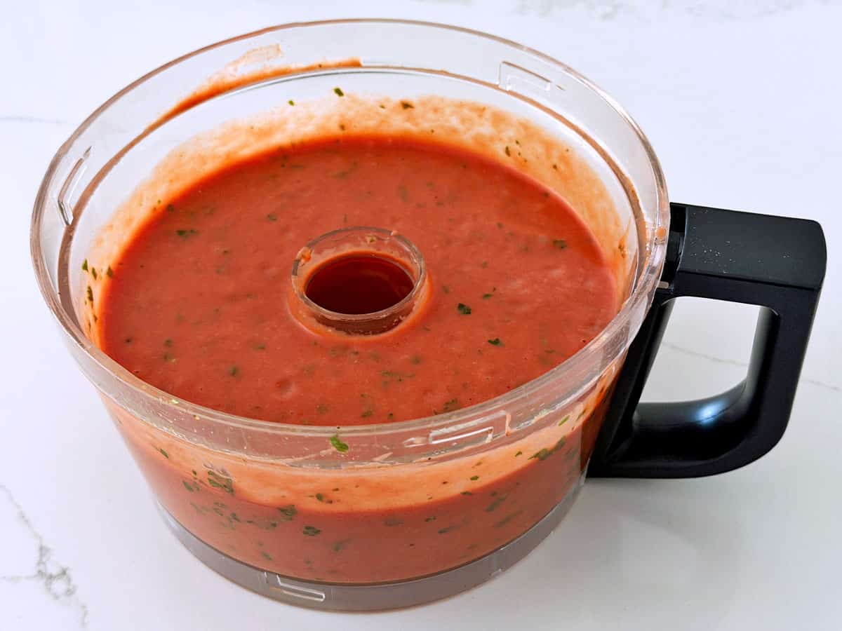 Cold tomato soup reaches the edge of the food processor bowl.